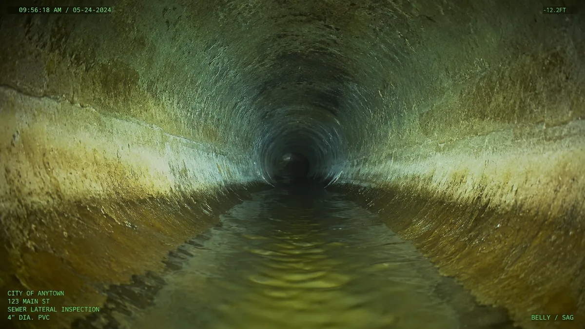 Inside an aged sewer pipe with a low belly section holding standing waste water