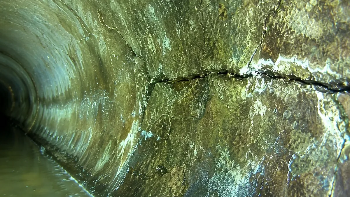 Inside an aged sewer pipe showing a hairline crack and fracture with mineral staining